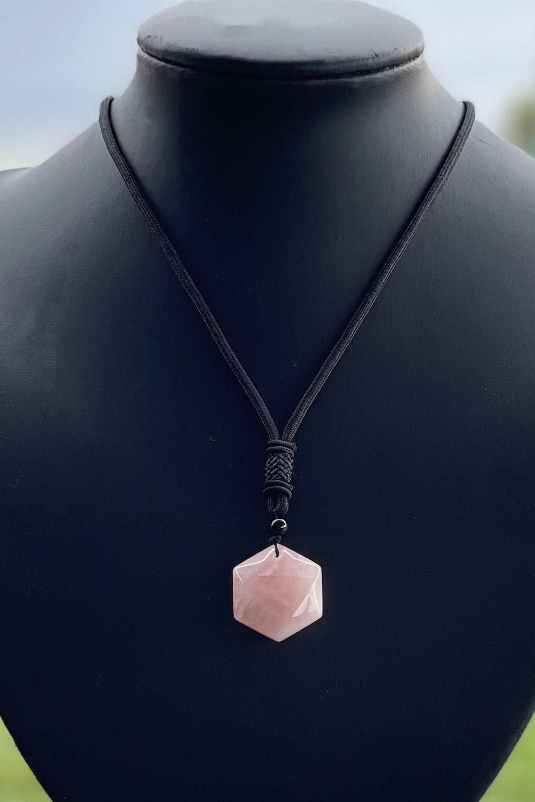 A hexagonal piece of rose quartz on a black cord necklace